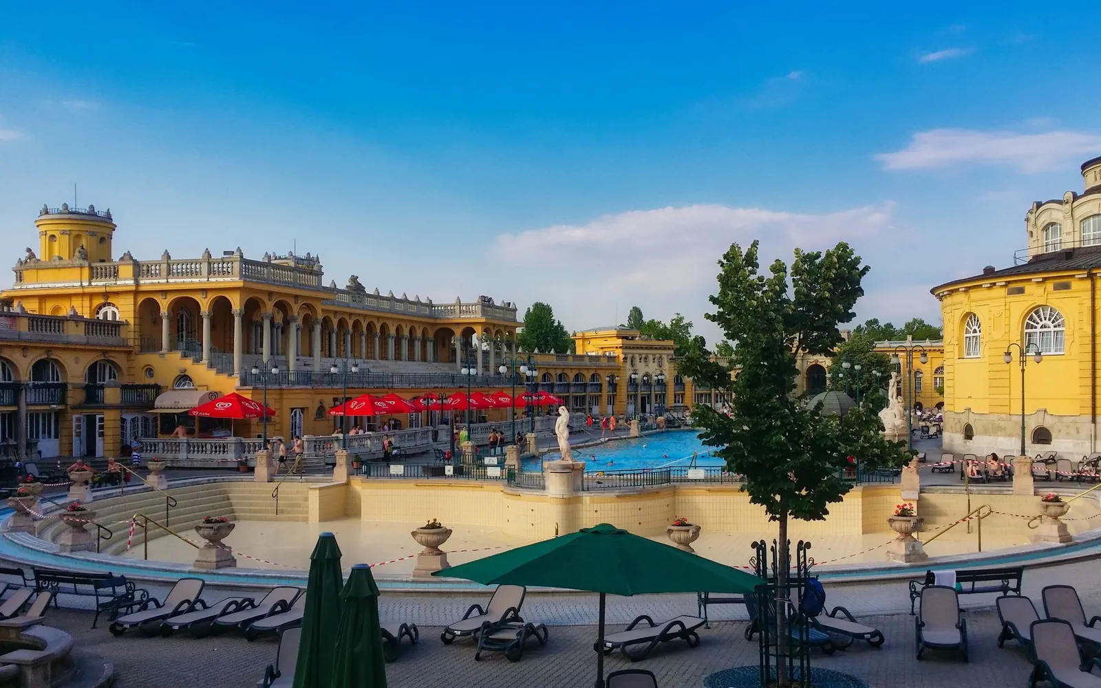 The yellow facades and outdoor pools of a historic Budapest thermal bath on a sunny day